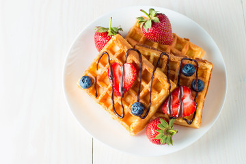 Photo of fresh homemade food made of berry Belgian waffles with honey, chocolate, strawberry, blueberry, maple syrup and cream. Healthy dessert breakfast concept with juice. 