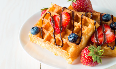 Photo of fresh homemade food made of berry Belgian waffles with honey, chocolate, strawberry, blueberry, maple syrup and cream. Healthy dessert breakfast concept with juice. 