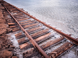 Rusty razy rails and rotten sleepers covered of salt on old railroad tracks on a mound at salt...