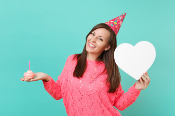 Smiling young woman in knitted pink sweater birthday hat hold in hand cake with candle, white heart...