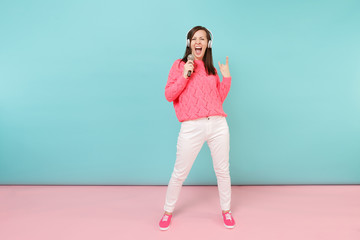 Full length portrait fun woman in knitted sweater, white pants, headphones sing song in microphone...