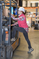 female worker climbing into cab of forklift truck
