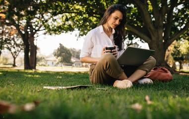 Obraz premium Woman at park with coffee watching video on laptop