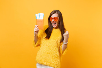 Overjoyed young woman in orange heart glasses screaming, doing winner gesture holding passport...