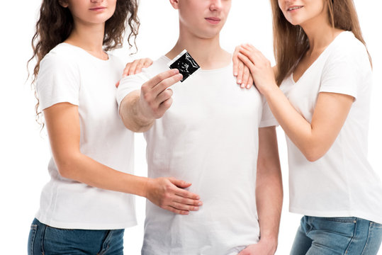 cropped image of man showing condom, two girls hugging him isolated on white, world aids day concept