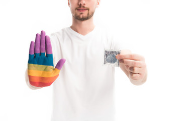 cropped image of homosexual man with hand painted in rainbow holding condom isolated on white,...
