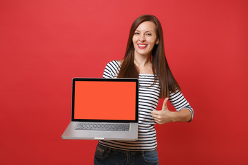 Beautiful young woman showing thumb up, holding laptop pc computer with blank black empty screen isolated on bright red wall background. People sincere emotions, lifestyle concept. Mock up copy space.