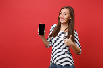 Portrait of beautiful young woman showing thumb up holding mobile phone with blank black empty screen isolated on bright red background. People sincere emotions, lifestyle concept. Mock up copy space.