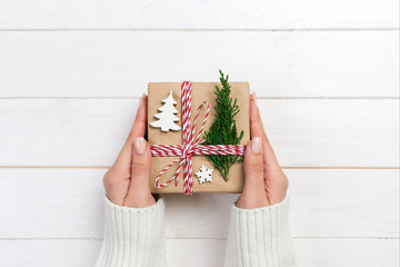 Woman hands give wrapped christmas handmade present in paper with christmas decoration. Present box on holiday on dark wooden table, top view