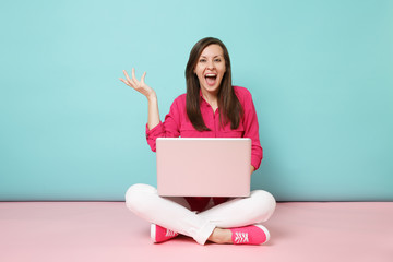 Full length portrait of young woman in rose shirt blouse white pants sitting on floor using laptop pc isolated on pink blue pastel wall background studio. Fashion lifestyle concept. Mock up copy space