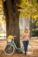 Young woman with bicycle using smartphone in autumn park