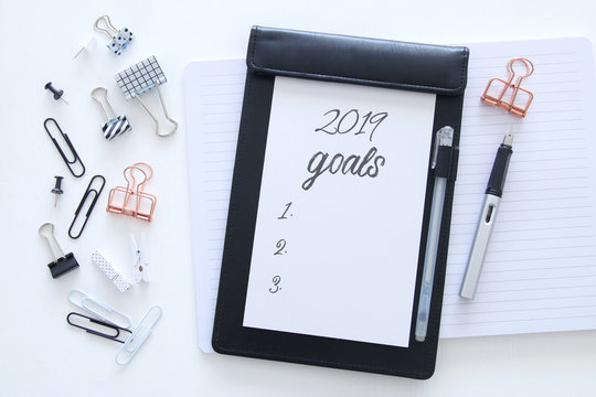 Top view 2019 goals list with notebook over wooden white desk.