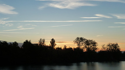 Fototapeta premium Sunrise on the lake over the forest. Illuminated sky with light clouds.