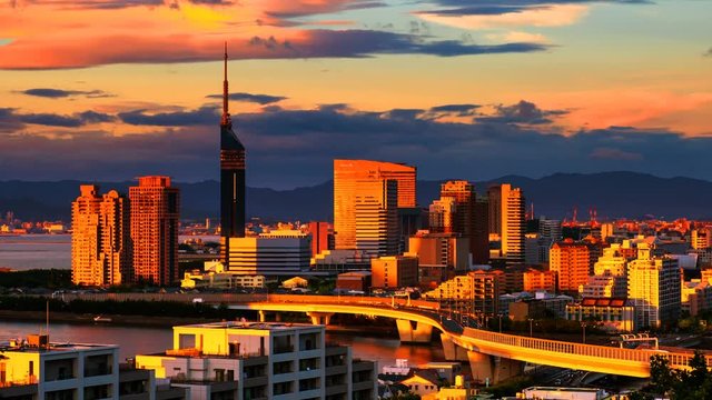 Fukuoka, Japan. A sunset video with a view of central Fukuoka, Japan, with tall modern buildings standing by the Hakata Bay on a cloudy summer day. Time-lapse from day to night, zoom in