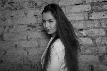 Black and white portrait of a young woman on a brick background. 