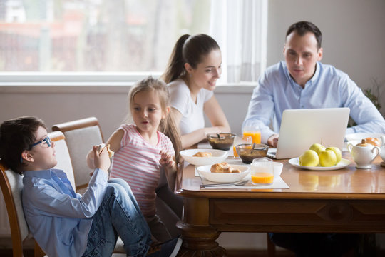 Whole Family Sitting At Dining Table In Kitchen After Breakfast At Home. Married Couple Reading News On Pc Little Kids Have Fun With Smartphone. People Addicted With Gadgets Devices Bad Habit Concept