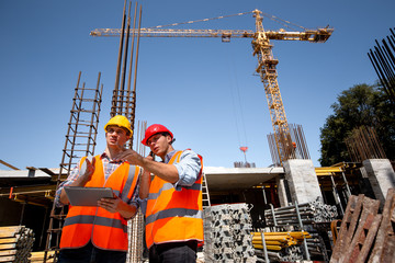 Structural engineer and architect dressed in orange work vests and  hard bats  discuss the...