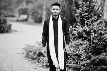 Indian stylish man in black traditional clothes with white scarf posed outdoor.