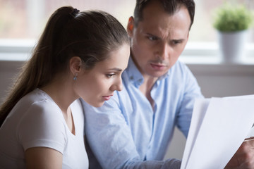 Stressed spouses read letter document notification about unpaid bills taxes or unexpected expenses or due debt. Couple feels frustrated and confused. Bankruptcy lack of money financial problem concept