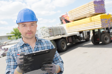 Man with clipboard, forklift unloading lorry in background