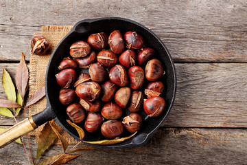 Roasted chestnuts in a pan on a wooden background. top wiev.