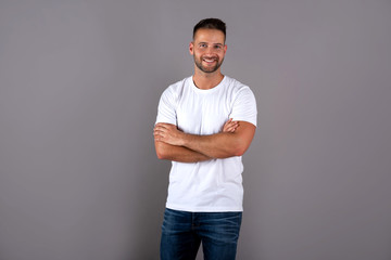 A smiling handsome young man in a white tshirt standing in front of a grey background in the studio.