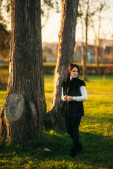 Dark haired woman stand in front of tree. Woman has bob haircut