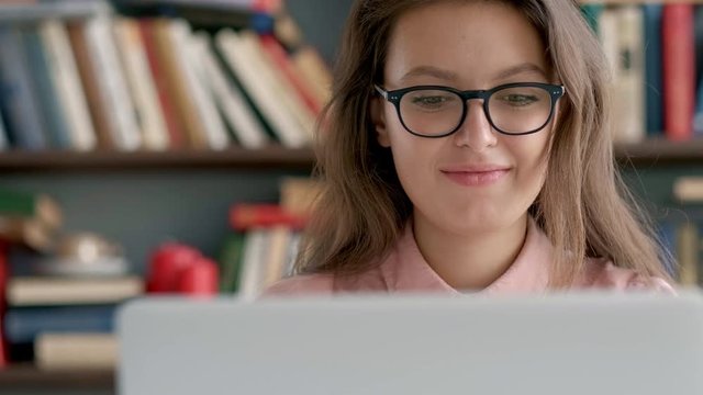 College student works on essay at the library. Attractive Hispanic woman with glasses reading book and typing on computer. 4k