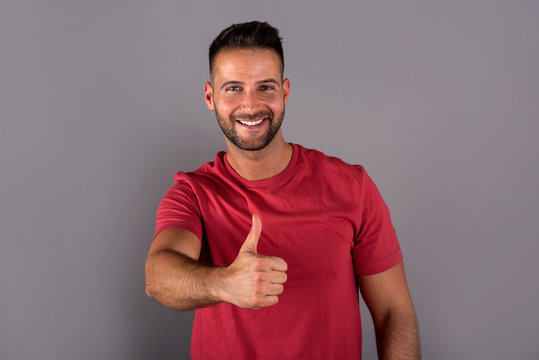 A Smiling Handsome Young Man In A Red Tshirt Standing In Front Of A Grey Background In The Studio.