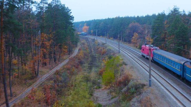 Aerial following shot of two trains - freight and suburban - go towards each other in the autumn forest