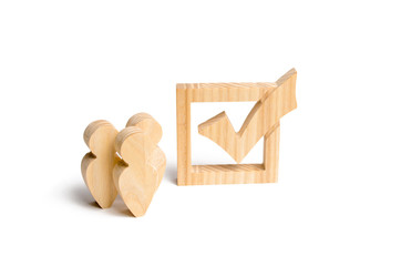Three wooden human figures stand together next to a tick in the box. The concept of elections and social technologies. Volunteers, parties, candidates, constituency electorates. Human rights.