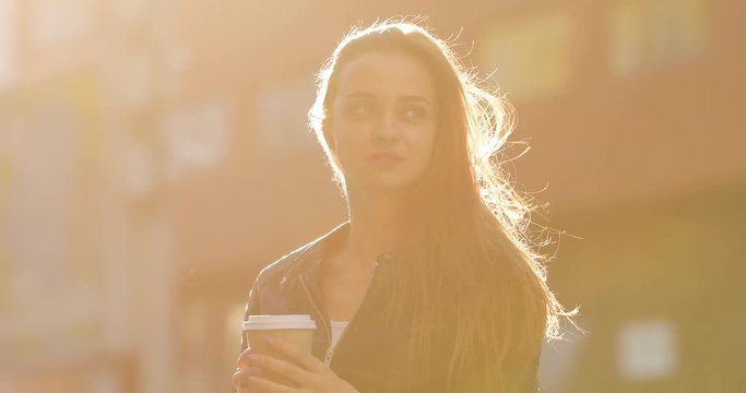 Silhouette of woman holding coffee cup in city, sunlight, strong wind