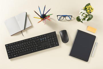 Top view of desk with tablet and pen, flowers, keyboard and mouse, booklet, automatic pencil, stick note, glasses and color pencil, on a clean background