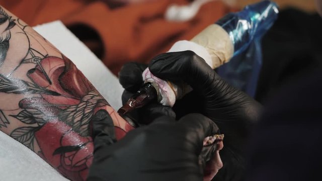 Macro view of professional tattoo master is painting with red ink, making cover. Works in black sterile latex gloves with handmade rotor gun machine in studio. Slow motion