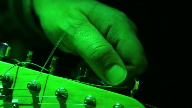 The hand of a man adjusts pegs of an electric guitar.