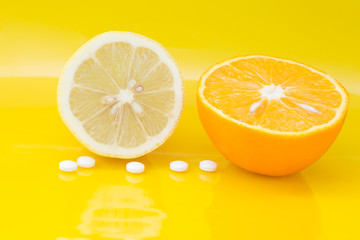 Vitamin C during during cold and flu season . Lemon half orange half and vitamin C tablets on yellow background