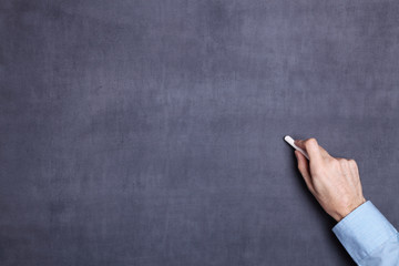 Hand holding a piece of white chalk and ready to start writing or drawing on a blackboard