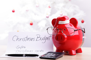 Piggy bank wearing glasses and Santa hat with a Christmas budget plan