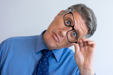 Crazy businessman fooling at camera. Closeup of middle aged Caucasian man touching askew glasses and grimacing. Crazy face expression concept