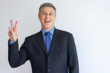 Happy businessman enjoying success. Cheerful mid adult Caucasian man in jacket showing victory sign. Achievement concept