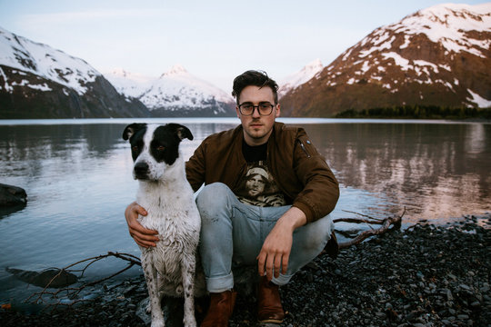 A man and his dog with snow capped mountains and a lake in the background