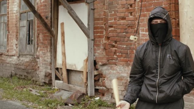Hooliganin black mask and jacket with hood holds in baseball bat on street