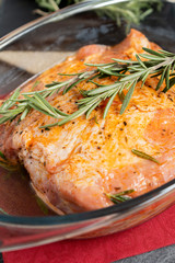 Pork raw meat in glass bowl ready for baking. Close up of preparing meat with rosemary herb. Rural cooking concept.