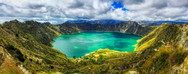 Foto op Canvas A bird's eye panoramic view of the bright green volcanic Quilotoa Lake in Ecuador with lots of white and grey clouds in a blue sky and green brush on the side of the caldera © FletchJr Photography