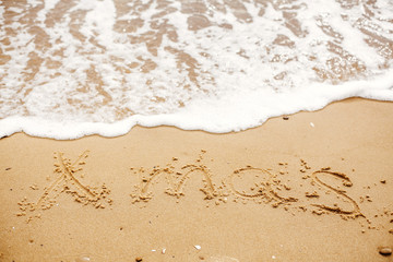 Xmas text written on sandy beach with wave near sea. Travel and vacations. Space for text. Merry Christmas concept, happy holidays.