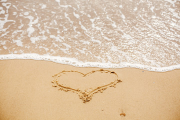 Heart written on sandy beach with wave near sea. Love concept. Happy valentine's day.  Honeymoon for newlyweds. Valentine day. Space for text. Happy holidays