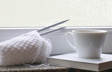 White woolen knitting, book and tea mug on the windowsill. Winter time concept