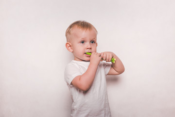 Handsome little boy in white brushing his teeth with a toothbrush.