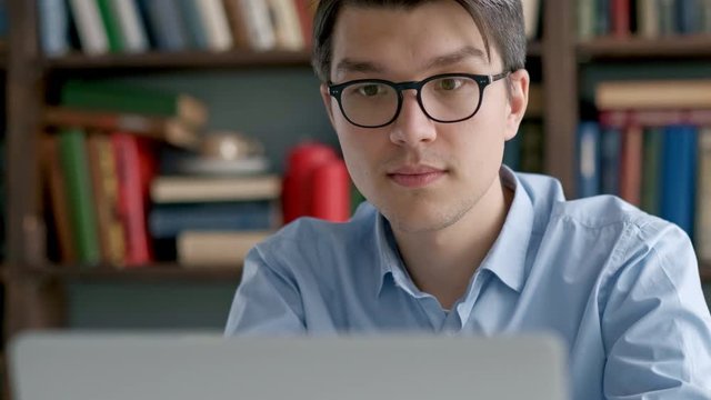 Male university student looking at laptop screen thoughtfully while doing homework. Closeup of concentrated boy trying to fulfill difficult task while studying
