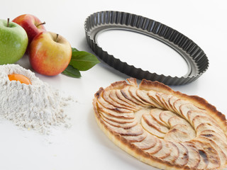 Bodegón compuesto por un molde rizado, un pastel de manzana, manzanas, harina y huevo